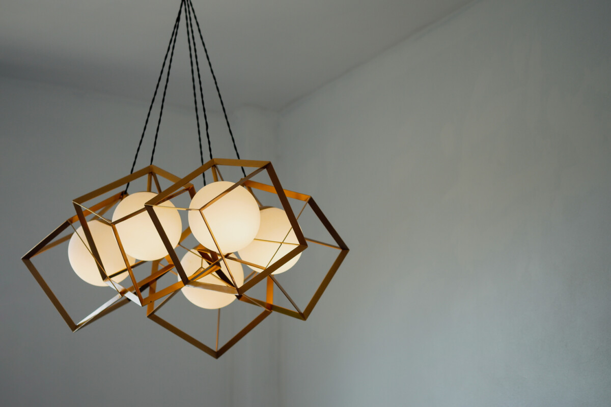 A round lamp with a rectangular iron frame suspended from the ceiling, illuminating in gold. 