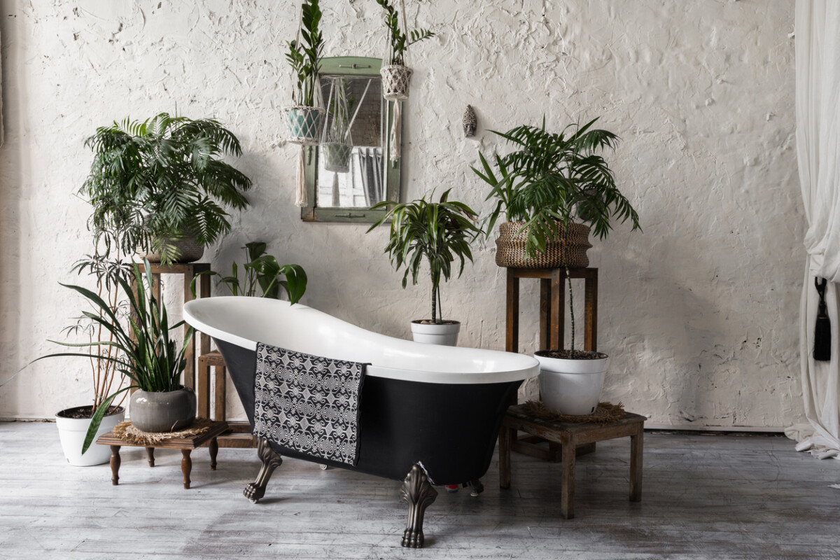 Modern bathroom with freestanding bathtub, wooden and botanical accents, and large windows in a minimalist interior.