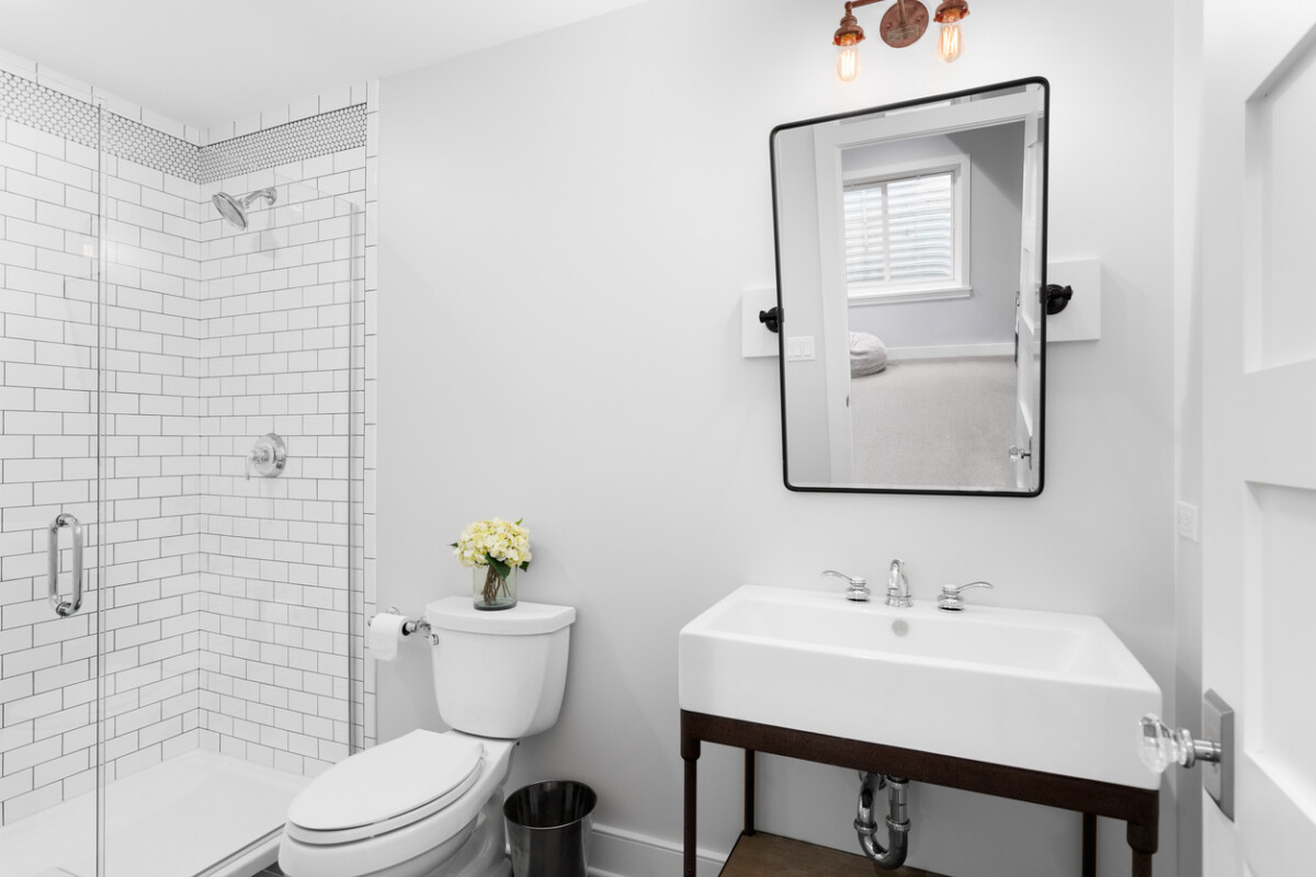 Modern farmhouse bathroom with a pedestal sink and tiled shower, featuring rustic accents and natural light.