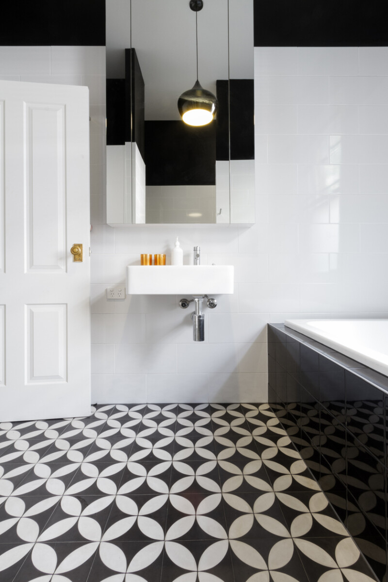 Luxury monochrome bathroom with patterned floor tiles, freestanding bathtub, and minimalist fixtures.